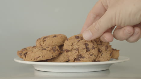 Hand-grabbing-chocolate-chip-cookies-on-a-white-plate
