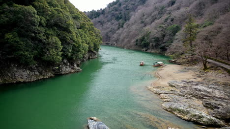 Filmische-Drohnenaufnahme,-Die-Einen-Fluss-Hinuntergeht,-Vorbei-An-Kleinen-Booten-In-Kyoto,-Japan