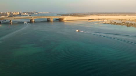 Weißes-Motorboot-Segelt-Türkisfarbenes-Ozeanflusswasser-Unter-Einer-Brücke,-Naher-Osten