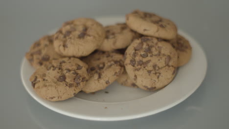 Hand-grabbing-chocolate-chip-cookies-from-a-white-plate---high-angle