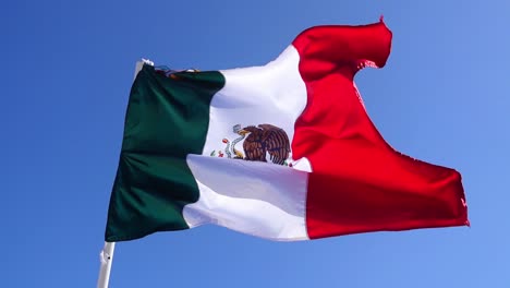 Resultado,-Vista-Panorámica-De-La-Bandera-Mexicana,-Ondeando-En-El-Asta-De-La-Bandera-En-Yucatán,-México,-Cielo-Azul-Brillante-En-El-Fondo