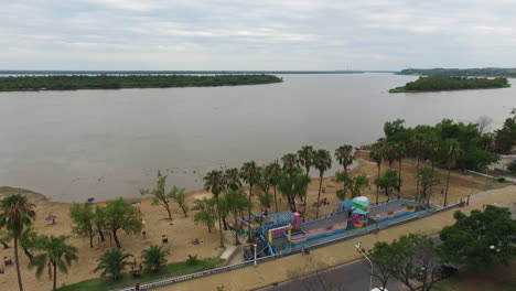 Aerial-View-of-Parana-City-River-and-Traffic-on-Coastal-Road-Under-Urquiza-Park,-Islands-in-Green-Lush-on-Cloudy-Summer-Day,-Argentina