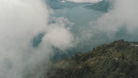 Drone-aerial-flying-high-over-the-clouds,-mountain-cliff-with-trees-revealing-lake-Atitlan,-Guatemala