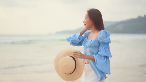 Young-Asian-woman-walks-on-beach-and-puts-her-hat-on