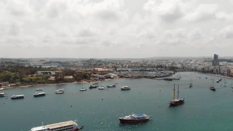 Aerial-4k-drone-footage-panning-from-a-harbor-with-anchored-sea-vessels-and-revealing-a-cityscape-of-the-Mediterranean-island-town-of-Sliema,-Malta