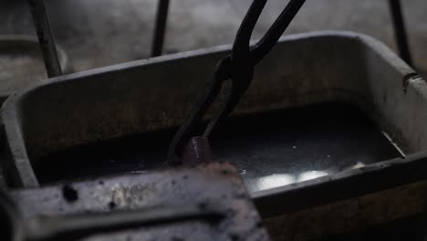 Close-up-of-a-blacksmith-putting-hot-metal-into-water-to-cool,-a-process-known-as-quenching