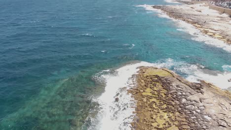 Rocky-Seafront-washed-by-the-Mediterranean-sea-in-the-city-of-Sliema,-Malta---Aerial-Tilt-up-Reveal-shot