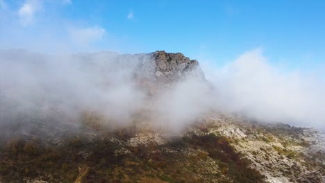 Drone-shot-of-a-mountain-peak-covered-in-fog-in-an-autumn-sunny-day-with-blue-sky
