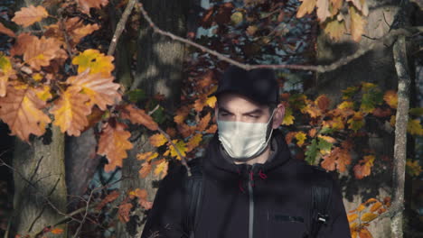 Male-tourist-wearing-face-mask-in-forest-walking-towards-camera,-covid-pandemic-symbolism,-middle-front-closeup-shot