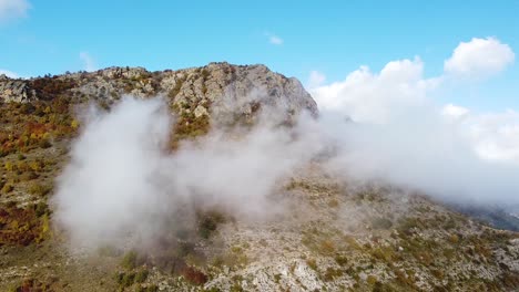 Drohnenaufnahme-Eines-Felsigen-Berggipfels,-Der-An-Einem-Sonnigen-Tag-Mit-Nebel-Bedeckt-Ist