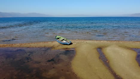 Abandoned-fishing-boat-on-sandy-shore-of-mountain-lake-in-Pogradec,-Albania