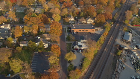 Aerial-of-Kirkwood-neighborhood-in-Fall-on-the-right-side-of-the-train-tracks-at-peak-color-tracking-left-over-pretty-houses,-trees,-and-streets-with-cars-driving-home