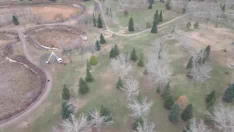 aerial-birds-eye-fly-over-dried-up-man-made-ponds-community-center-arbory-trimming-machinary-pruning-trees-at-a-park-on-a-full-afternoon-with-scattered-pine-trees-and-bare-maple-trees1-3