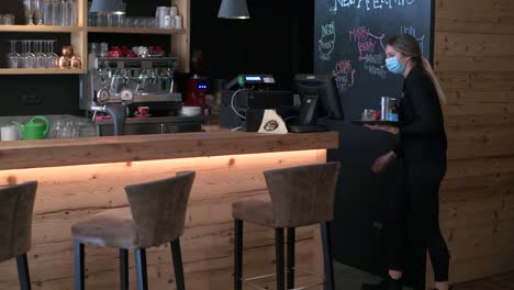 Waitress-with-face-mask-and-drinks-on-a-tray,-walks-behind-the-counter