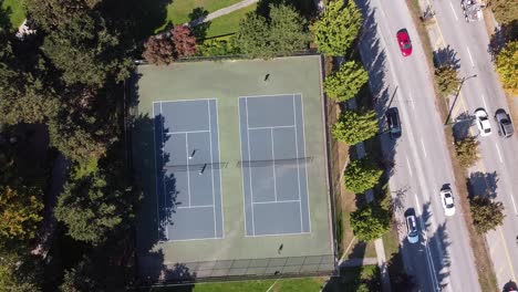 1-2-Aerial-hold-top-birds-eye-view-top-of-couples-playing-tennis-at-a-modern-park-by-luxurious-neighbourhood-close-to-a-garden-road-freeway-with-light-traffic-at-tropical-home-town-in-the-hot-summer