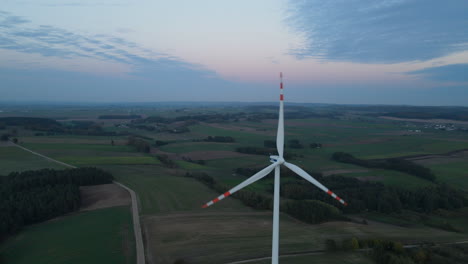 Rotierende-Windkraftanlage-Auf-Ackerland-Mit-Weiter-Landschaft-Und-Bunten-Wolken-Im-Hintergrund