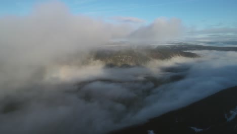 Zooming-out-drone-footage-of-a-valley-covered-by-clouds-at-sunrise
