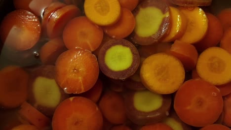 Chopped-Heirloom-Carrots-boiling-in-water,-close-up,-slow-zoom-in