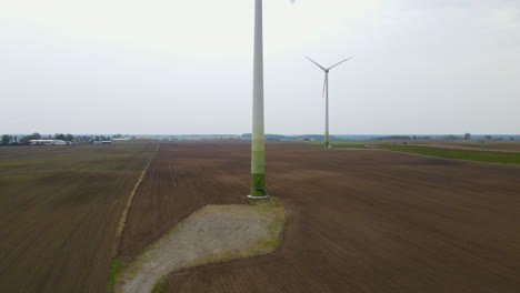 Ascending-aerial-shot-of-spinning-wind-turbine-standing-on-soil-field-on-cloudy-day