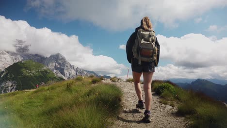 Blick-Von-Hinten-Auf-Eine-Wandertouristin-Mit-Rucksacktrekking-Und-Wandern-Auf-Einem-Bergpfad-Mit-Den-Dolomiten-Im-Hintergrund