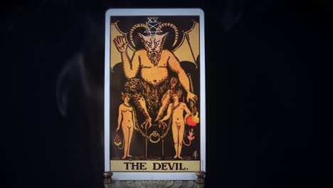 A-tarot-Devil-card-sits-on-a-brass-stand-as-smoke-rises-around-it