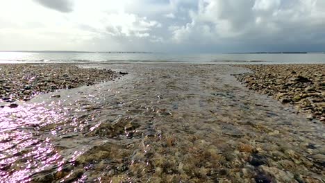 Coastal-river-flowing-over-pebble-beach-into-the-UK-sea