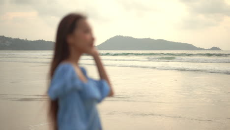 Rack-focus-from-the-background-beach-and-waves-rolling-on-to-a-pretty-young-woman-in-the-foreground-of-the-frame