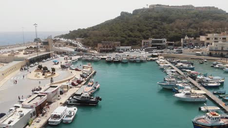 Puerto-De-Mgarr-Con-Embarcaciones-Ancladas-En-La-Escarpada-Costa-De-La-Isla-De-Gozo-En-Malta---Toma-Aérea-Sobrevolada
