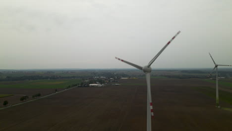 Two-Giant-Farm-Windmills-Spinning-In-The-Wind-Under-Gloomy-Sky-In-Poland---Drone-Shot