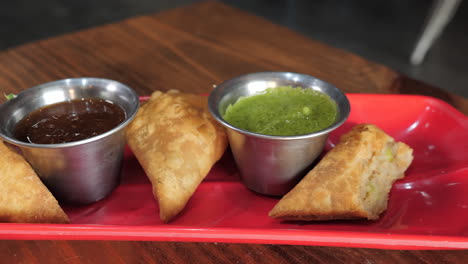 Samosas-dipped-in-cilantro-chutney-served-with-tamarind-chutney-on-red-plate,-slider-slow-motion-close-up-HD