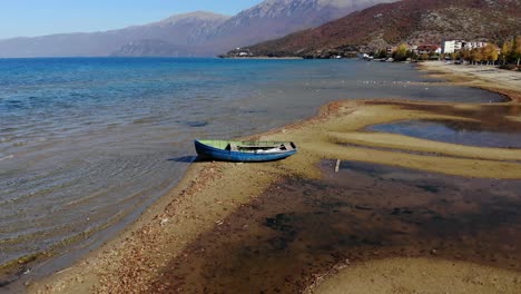 Barco-De-Pesca-En-La-Orilla-Del-Tranquilo-Lago-De-Ohrid-Con-Agua-Azul-Clara-Y-Fondo-De-Montañas