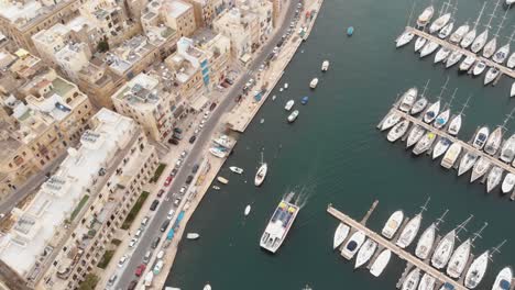 Bird's-eye,-panning-aerial-4k-drone-footage,-of-a-marina-along-a-water-channel-between-two-Mediterranean-cities-of-Malta