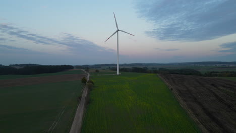 Aerial-view-of-wind-turbines-rotate-on-ecological-agricultural-field-under-blue-sunny-sky-with-sunset-on-background