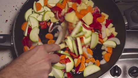 Man-stirs-vegetables-in-frying-pan-for-Spanish-pisto-with-wooden-spoon