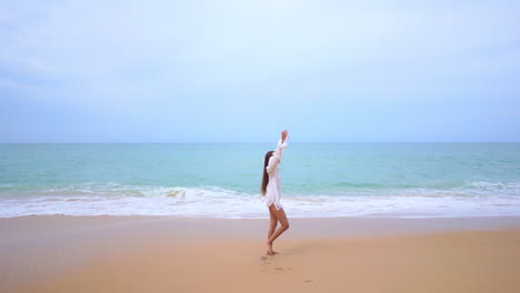 Young-woman-on-seashore-expresses-freedom-concept-by-raising-arms-and-looking-at-horizon