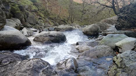 Rocky-waterfall-river-creek-flowing-over-boulders-in-seasonal-Autumn-woodland-slow-left-dolly