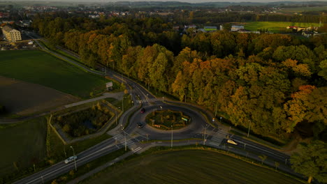 Kreisförmige-Kreuzung-In-Lubawa,-Polen---Fahrzeuge,-Die-Bei-Sonnenuntergang-Auf-Einer-Kreisverkehrstraße-Neben-Einem-Park-Mit-üppigen-Herbstbäumen-Fahren