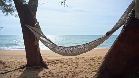 An-empty-hammock-hung-between-two-trees-shifts-in-the-breeze-over-the-sand-of-an-empty-beach