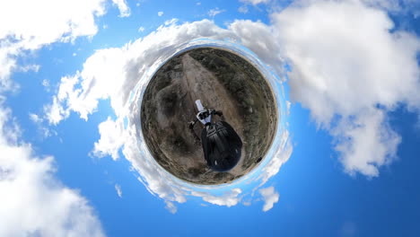Person-riding-a-dirt-bike-or-motorcycle-on-a-tiny-planet-with-a-blue-sky-and-cloudy-atmosphere