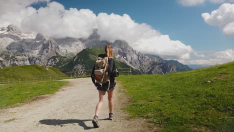 view-from-behind-of-a-hiker-tourist-traveler-woman-with-backpack-trekking-and-walking-on-a-mountain-path-with-the-dolomites-in-the-background