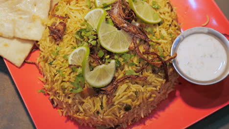 Authentic-biryani-naan-raita-topped-with-lime-slices-and-chilies,-overhead-slow-motion-HD