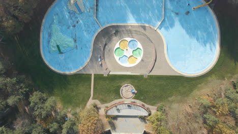 Top-down-aerial-of-deserted-outdoor-swimming-pool-surrounded-by-forest