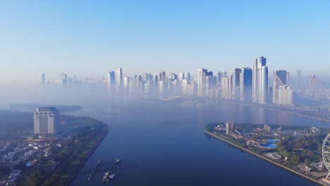 Aerial-View-of-Fog-over-Sharjah's-Lake,-Eye-of-Emirates,-Sharjah-Skyline-on-a-foggy-morning,-Fog-in-Gulf,-United-Arab-Emirates,-4K-Footage