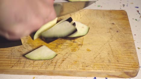 Closeup,-Hands-cuts-eggplant-slices-with-knife-on-wooden-cutting-board