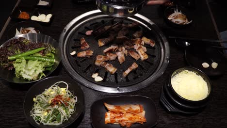 Grilling-Pork-Belly-Barbecue-With-Side-Dishes-On-The-Table---Samgyeopsal-Set-up---close-up,-high-angle