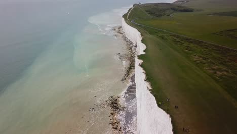 Tourists-walking-on-edge-of-Seven-Sisters-Beachy-Head-chalk-cliffs,-aerial