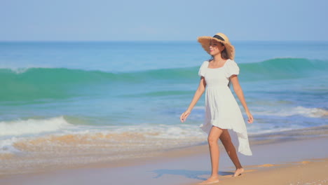 Young-woman-in-white-dress-and-hat-walks-barefoot-on-seashore