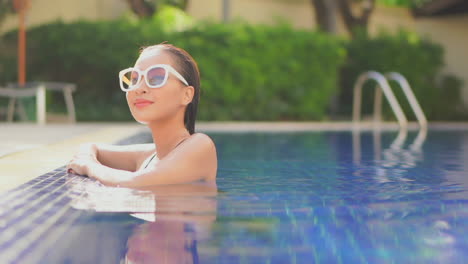 Beautiful-young-Asian-woman-with-big-sunglasses-relaxing-in-pool