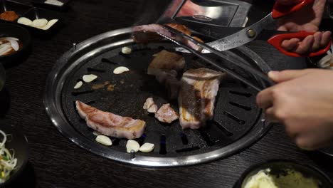 Cutting-Pork-Belly-With-Scissors-And-Tongs-At-Korean-Barbecue-Restaurant---close-up