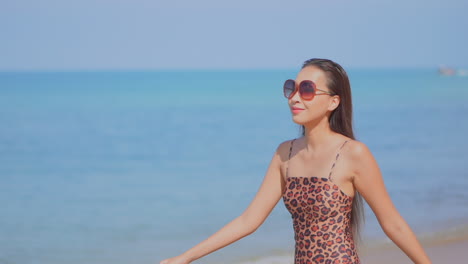 Medium-close-of-a-pretty-woman-in-a-leopard-print-bathing-suit-walks-along-a-deserted-beach-as-the-tide-comes-in